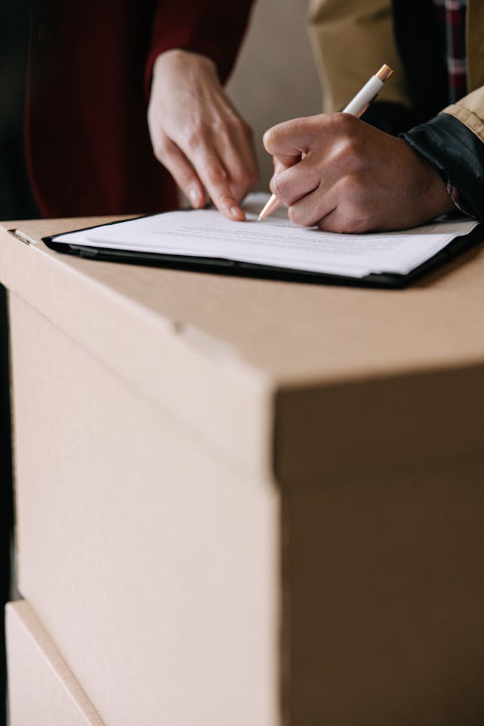 Hands signing lease documents on a cardboard box in an apartment.